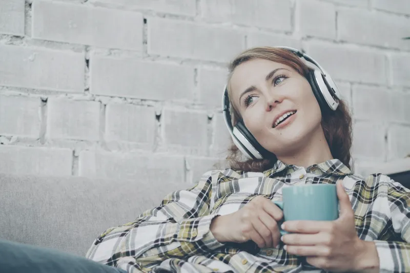 Eine Frau ruht sich mit Kopfhörern und einer Tasse auf dem Sofa aus.